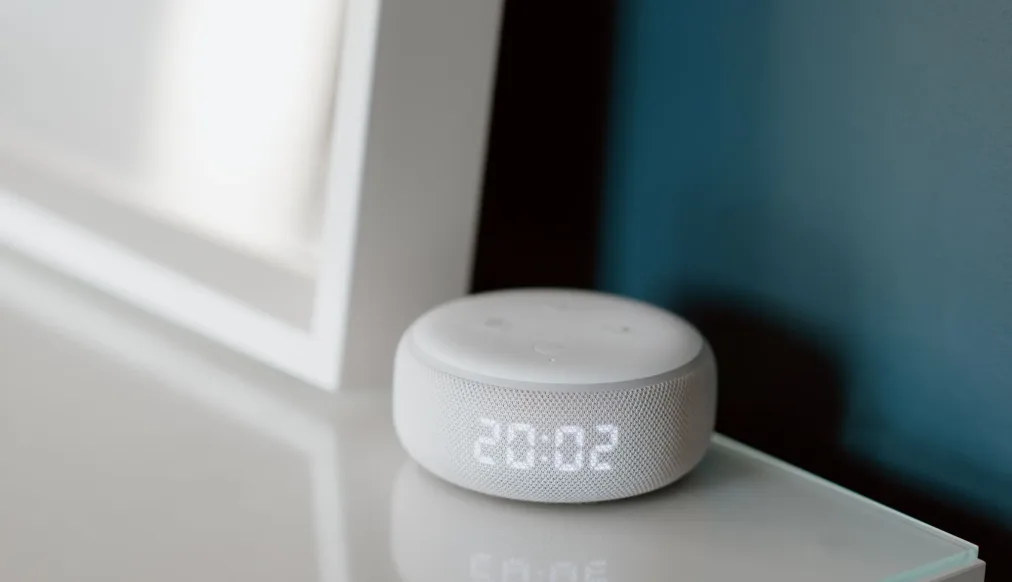Runder weißer smarter Lautsprecher auf einer Holzfläche im hellen Raum